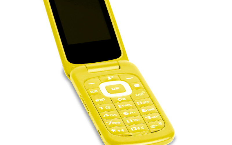 Close-up of a bright yellow flip phone featured in a jitterbug vs tracfone comparison for seniors